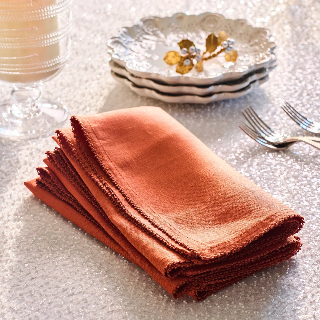 Folded rust linen napkins with decorative stitched edging styled on an elegant dining table