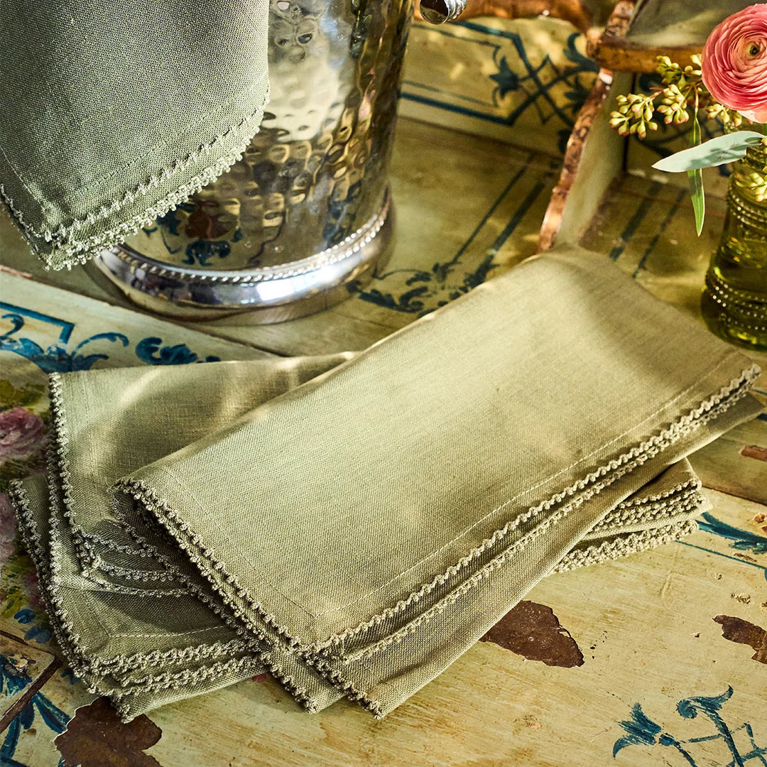 Stack of sage green linen napkins with crochet edging styled on a decorative table for elegant entertaining