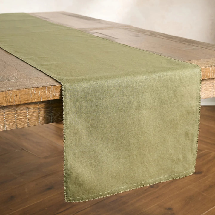 Sage green table runner with delicate crochet edging draped across a natural wood dining table