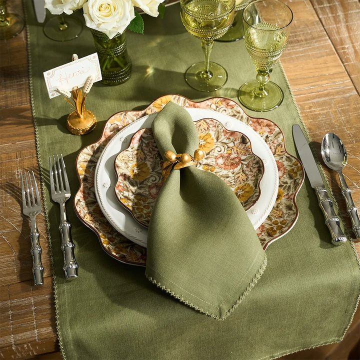 Sage green table runner styled with matching napkin, floral dinnerware, green glassware and gold accents for an elegant tablescape
