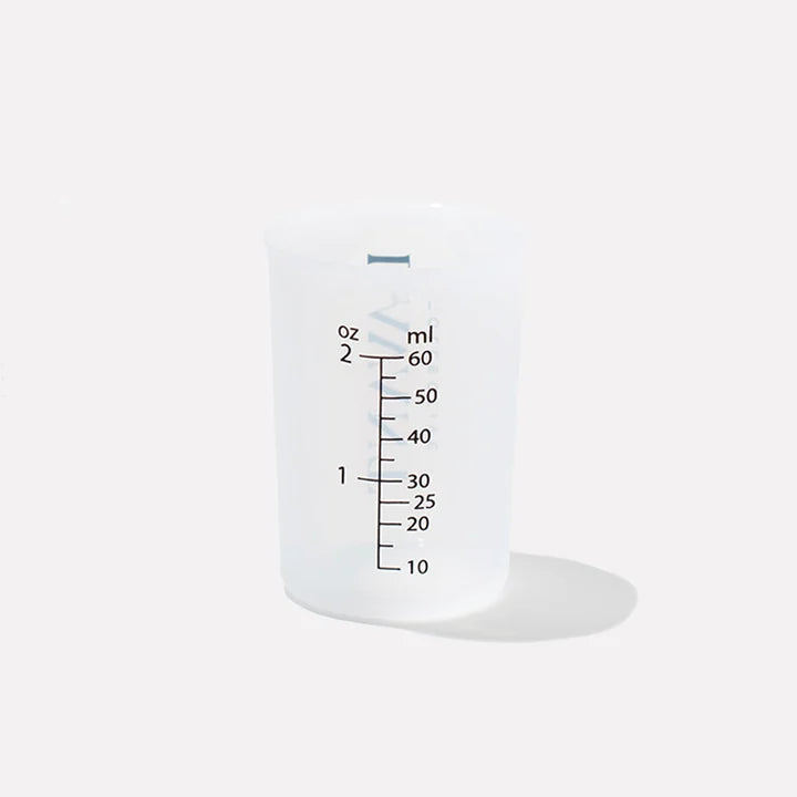 Translucent silicone laundry detergent measuring cup with ounce and milliliter measurement markings for portioning liquid detergent.