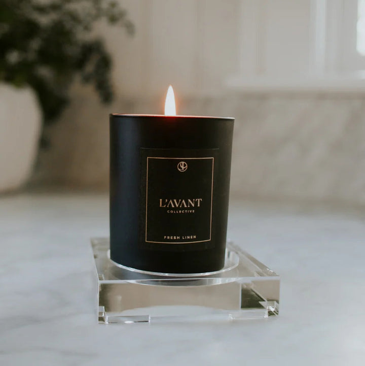 Small clear lucite display tray holding a black candle, creating an elevated candle display for a vanity, countertop, or tabletop