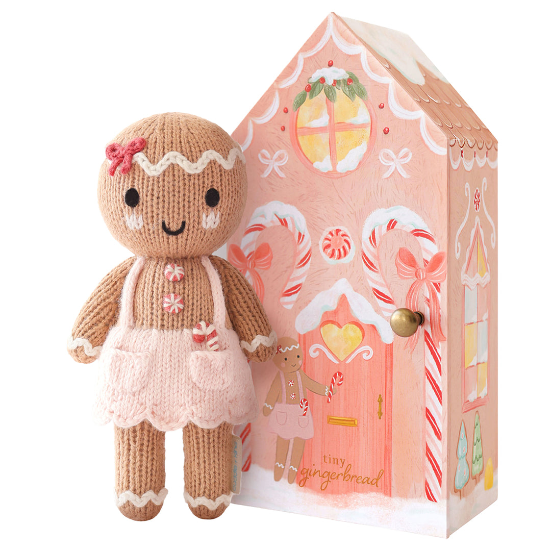 Tiny Gingerbread Sugarplum knit doll in a pink apron displayed beside a whimsical pink gingerbread house gift box