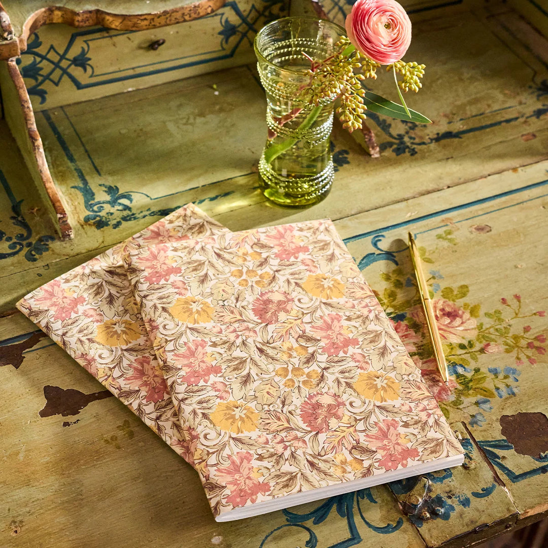 Vintage floral journal styled on an antique painted desk with a gold pen, pink flower and green glass vase.