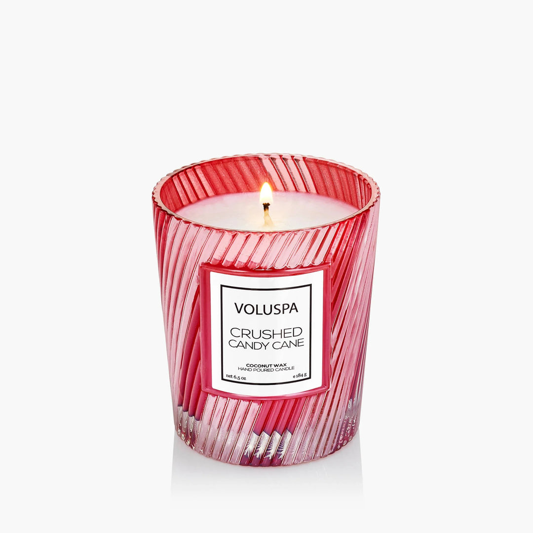 Lit Voluspa Crushed Candy Cane Classic Candle in decorative red and clear striped glass vessel