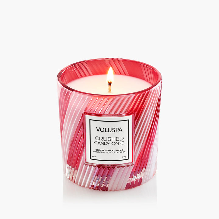 Lit Voluspa Crushed Candy Cane Luxe Classic Candle in decorative red and clear striped glass vessel