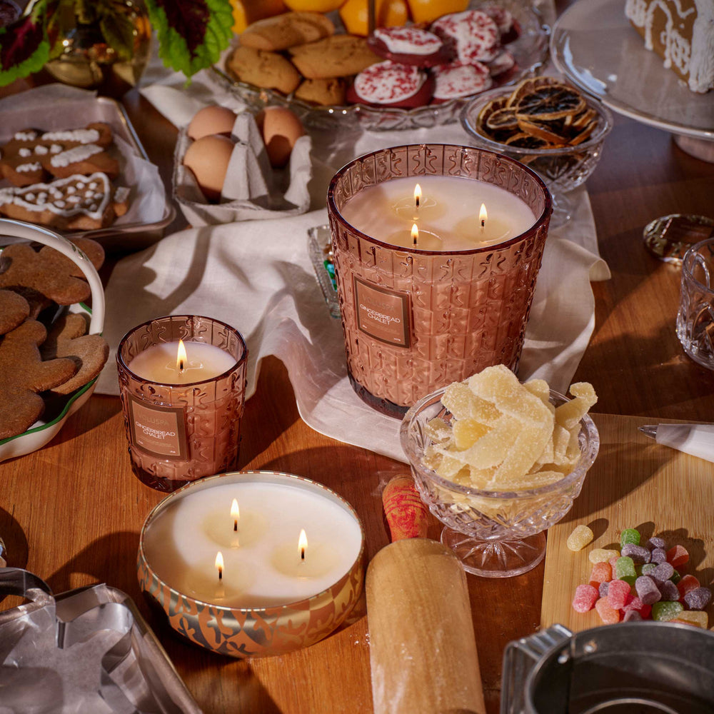 Lit Voluspa Gingerbread Chalet 3 Wick Hearth Candle displayed with festive gingerbread treats and holiday candles