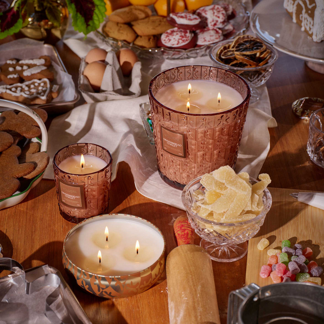 Lit Voluspa Gingerbread Chalet 3 Wick Hearth Candle displayed with festive gingerbread treats and holiday candles