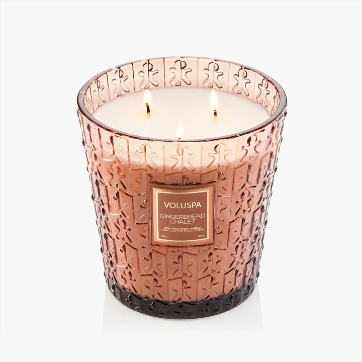 Lit Voluspa Gingerbread Chalet 3 Wick Hearth Candle with three wicks in embossed gingerbread glass