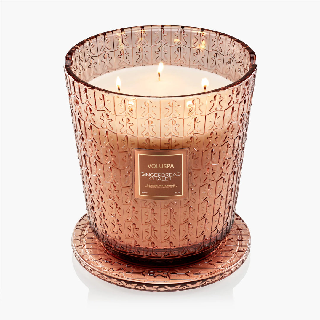 Lit Voluspa Gingerbread Chalet 5 Wick Hearth Candle in embossed glass with matching decorative base