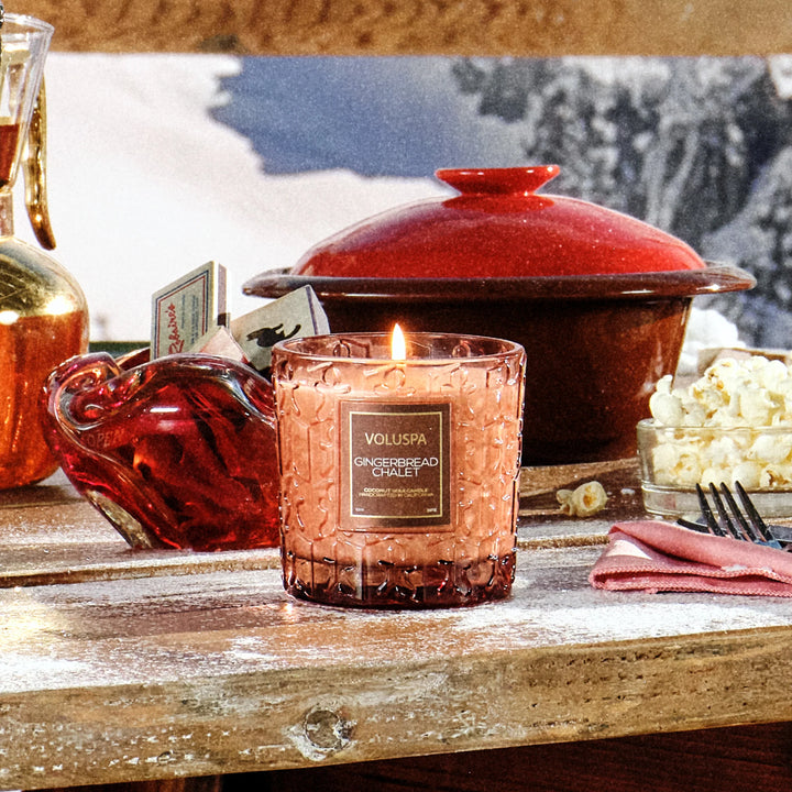Lit Voluspa Gingerbread Chalet Luxe Classic Candle displayed on a cozy holiday table