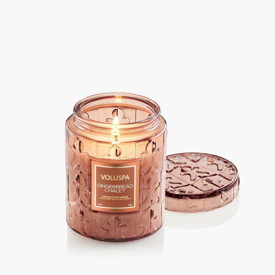 Lit Voluspa Gingerbread Chalet Small Jar Candle with embossed glass lid beside the jar