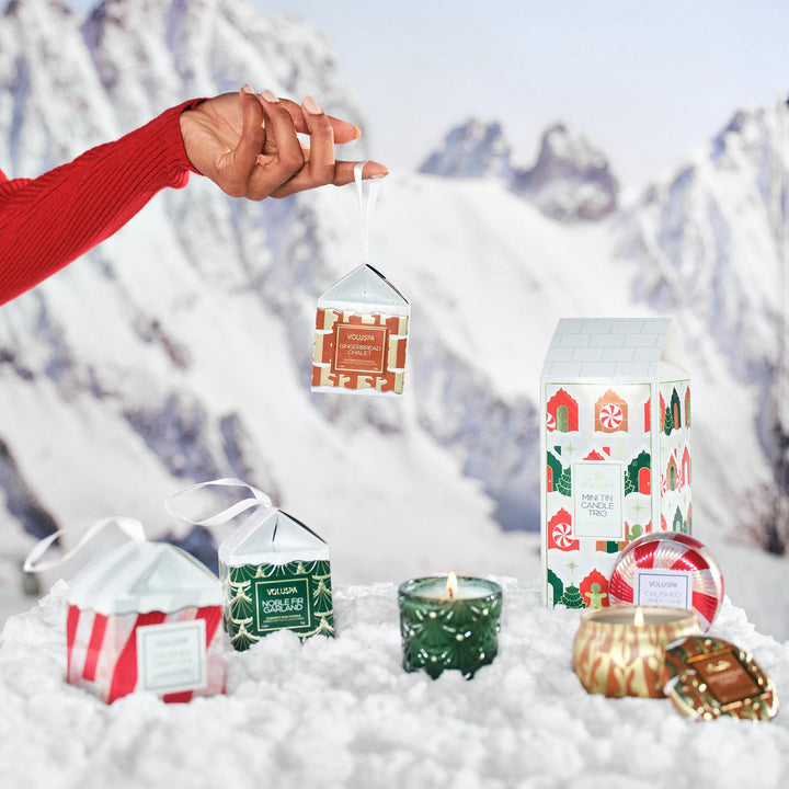 Voluspa Holiday Mini Tin Candle Trio displayed with festive Voluspa candles in a snowy Christmas setting