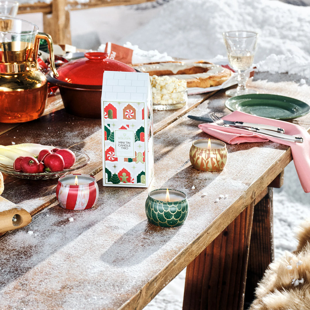 Voluspa Holiday Mini Tin Candle Trio displayed and lit on a festive winter holiday table