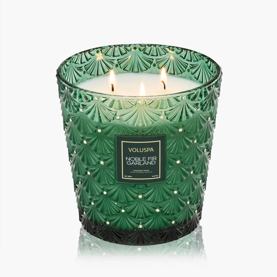 Voluspa Noble Fir Garland 38 oz 3 Wick Hearth Candle lit in an embossed emerald green glass vessel