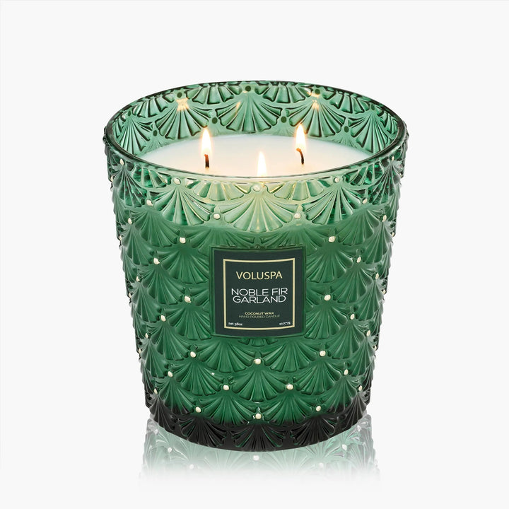 Voluspa Noble Fir Garland 38 oz 3 Wick Hearth Candle lit in an embossed emerald green glass vessel