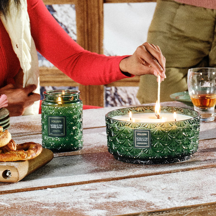 Voluspa Noble Fir Garland Centerpiece Candle glowing on a festive winter holiday table