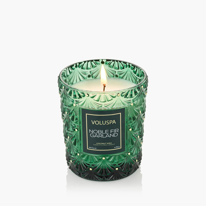 Lit Voluspa Noble Fir Garland Classic Candle in embossed emerald green glass with gold accents