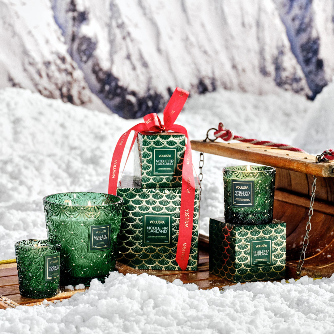 Voluspa Noble Fir Garland holiday candle collection styled with green gift boxes and red ribbon in the snow