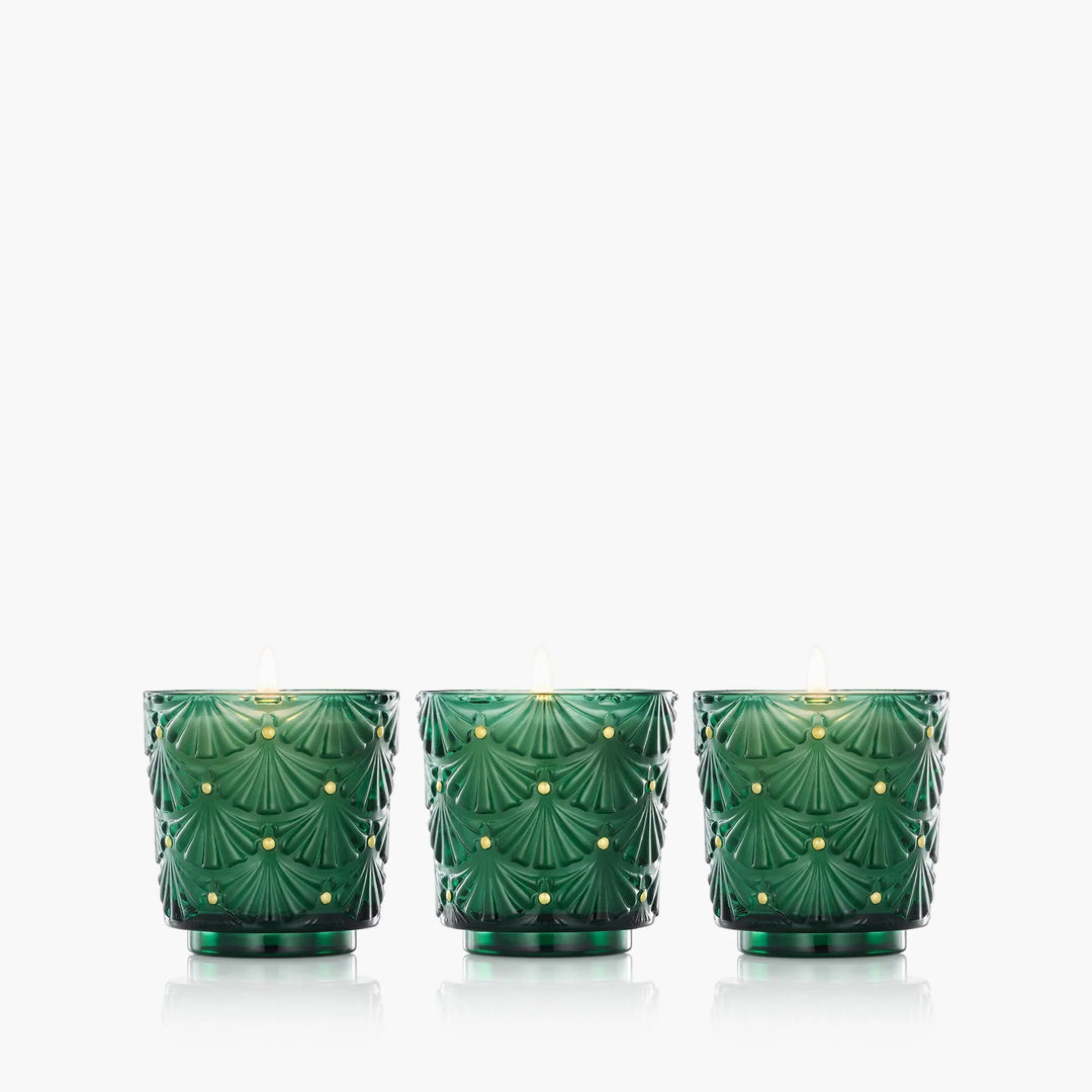 Three Voluspa Noble Fir Garland Mini Pedestal candles in embossed emerald green glass vessels with gold accents
