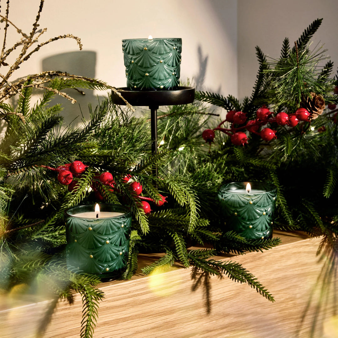Voluspa Noble Fir Garland Mini Pedestal Trio candles styled with evergreen branches and red berries for Christmas