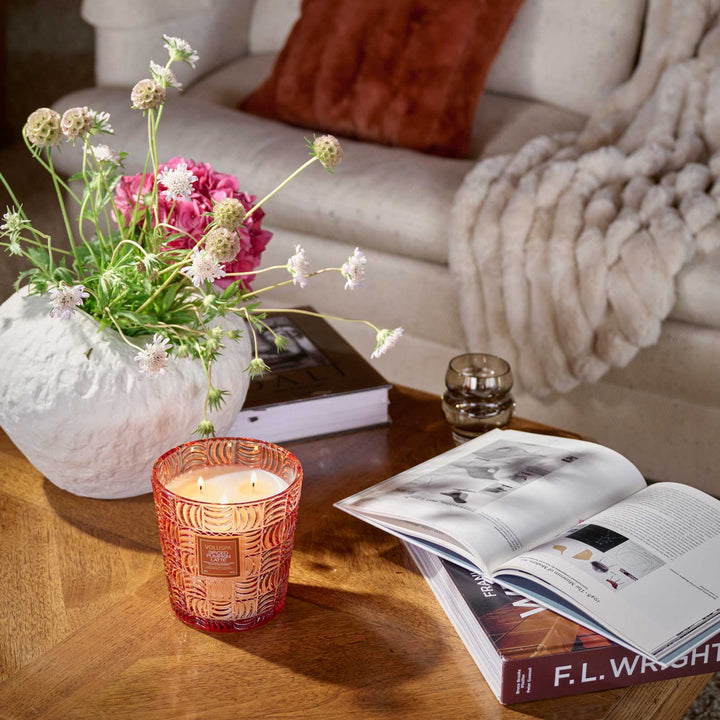 Lit Voluspa Spiced Pumpkin Latte 3 Wick Hearth Candle styled on a wooden coffee table with flowers and books