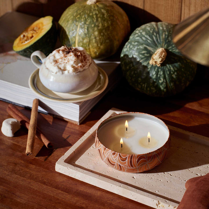 Lit Voluspa Spiced Pumpkin Latte 3 Wick Tin Candle styled with pumpkins, cinnamon sticks and a pumpkin latte