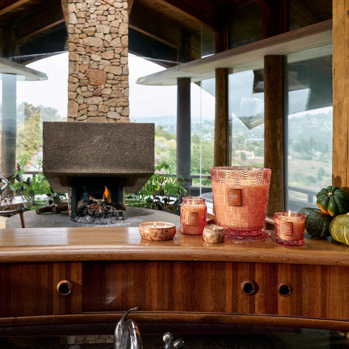 Voluspa Spiced Pumpkin Latte candle collection displayed with pumpkins near a cozy fireplace