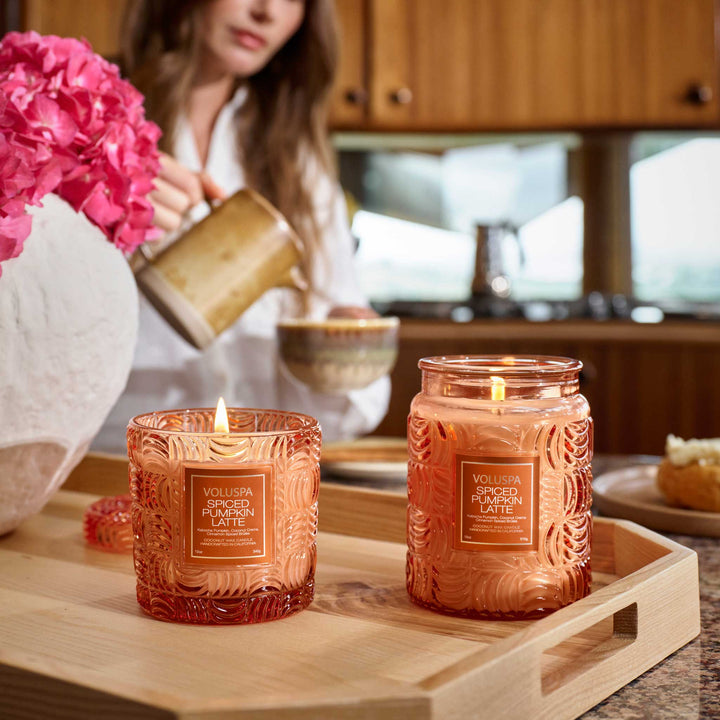 Voluspa Spiced Pumpkin Latte Large Jar Candle burning beside another candle on a wooden tray