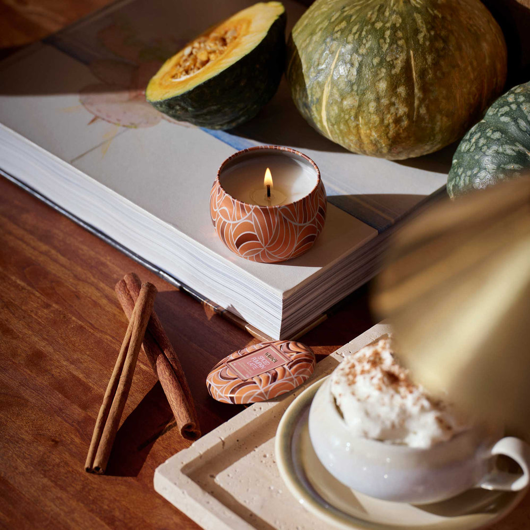 Lit Voluspa Spiced Pumpkin Latte Mini Tin Candle styled with pumpkins, cinnamon sticks and a pumpkin latte