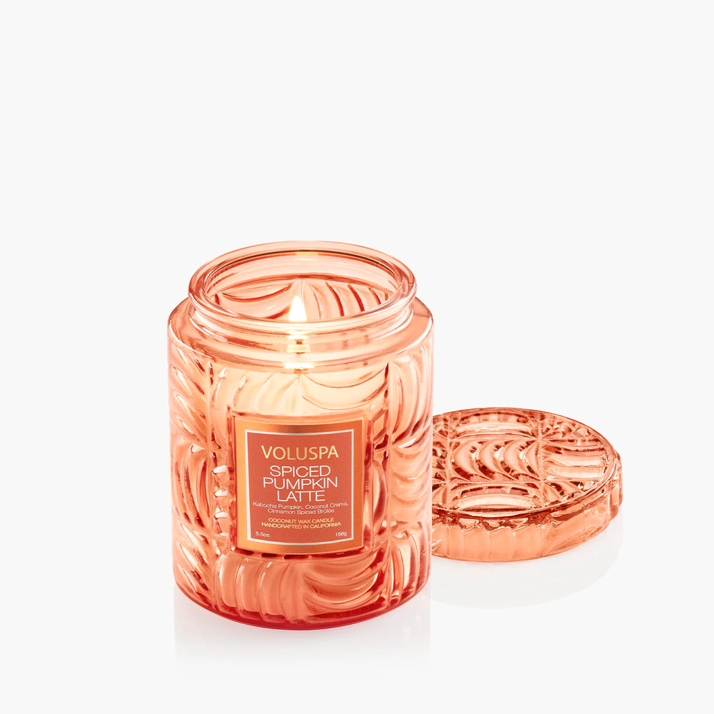 Lit Voluspa Spiced Pumpkin Latte Small Jar Candle with embossed orange glass lid beside it