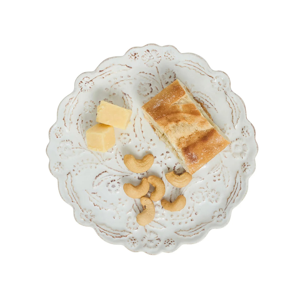 White floral appetizer plate with scalloped edges and raised botanical details styled with bread, cheese and cashews.