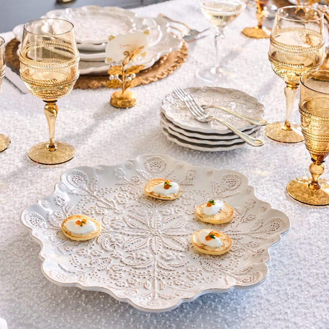 White floral round serving platter holding small appetizers on an elegant white and gold entertaining table.