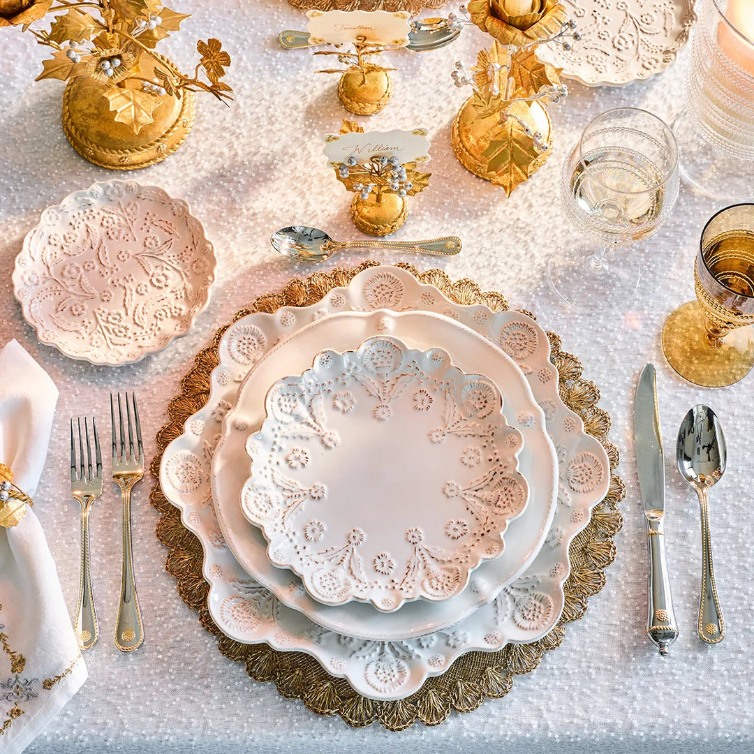 White floral round serving platter featured beneath layered scalloped dinnerware in an elegant gold and white place setting.
