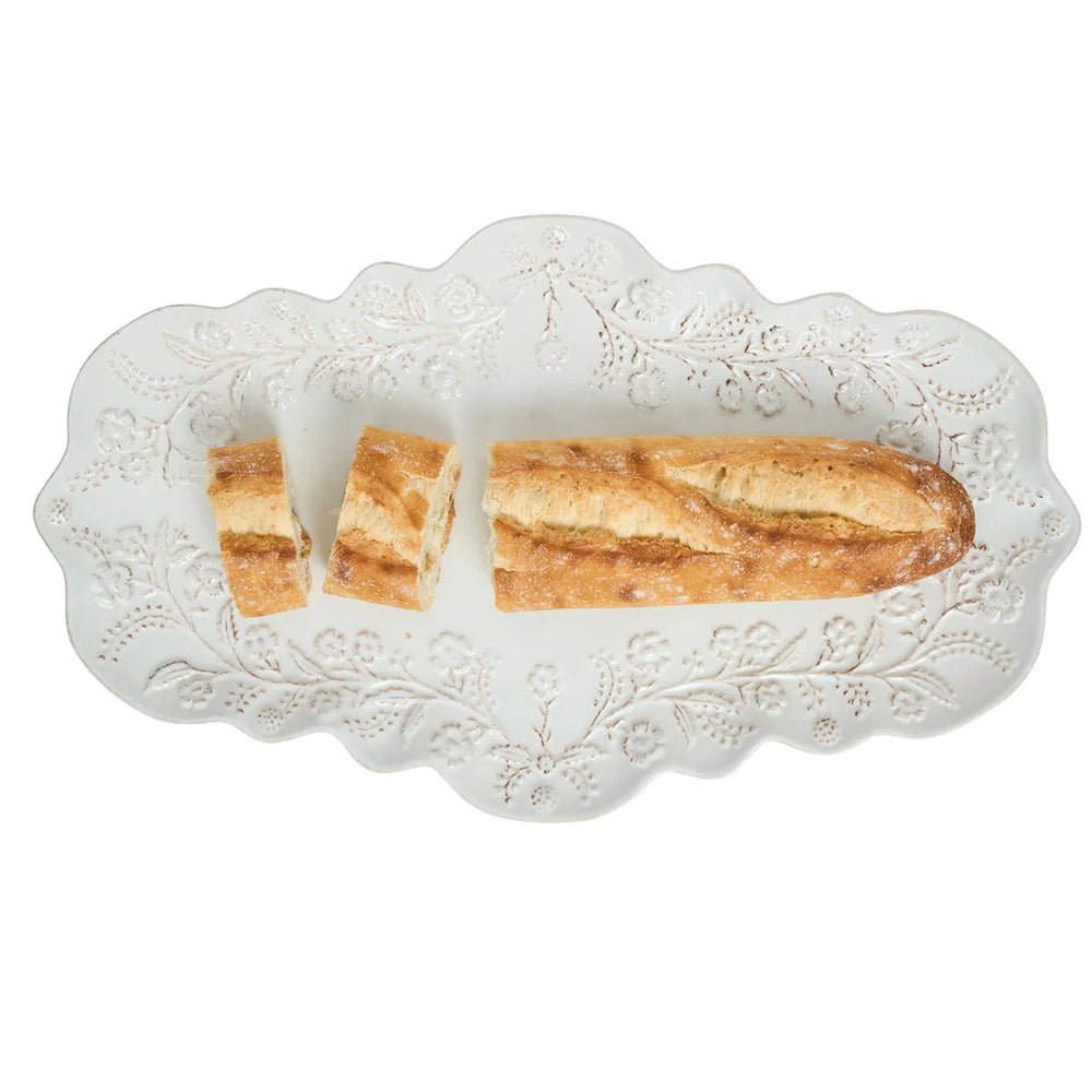 White floral serving platter with scalloped edges and raised floral details styled with sliced baguette bread.