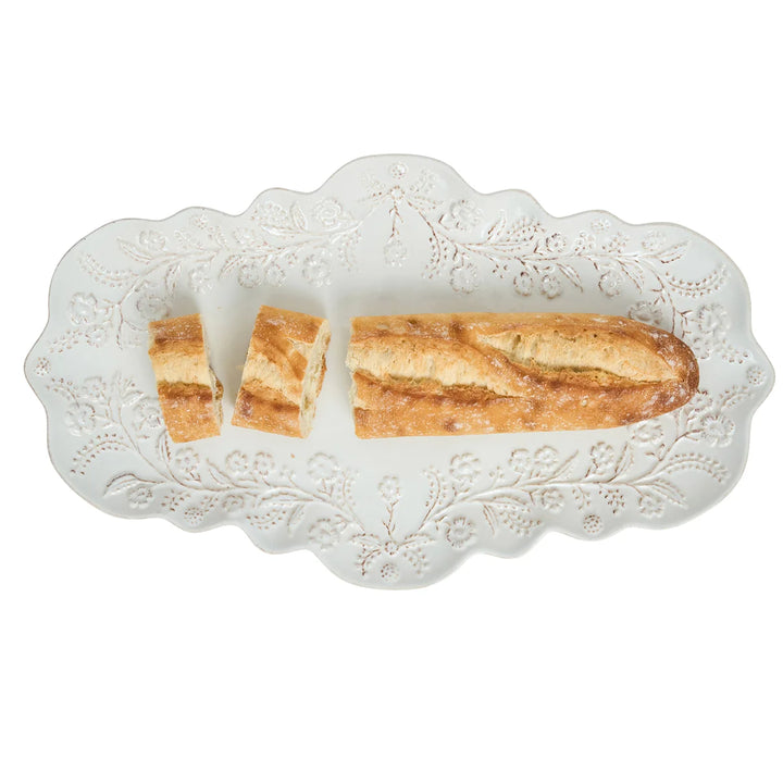 White floral serving platter with scalloped edges and raised floral details styled with sliced baguette bread.