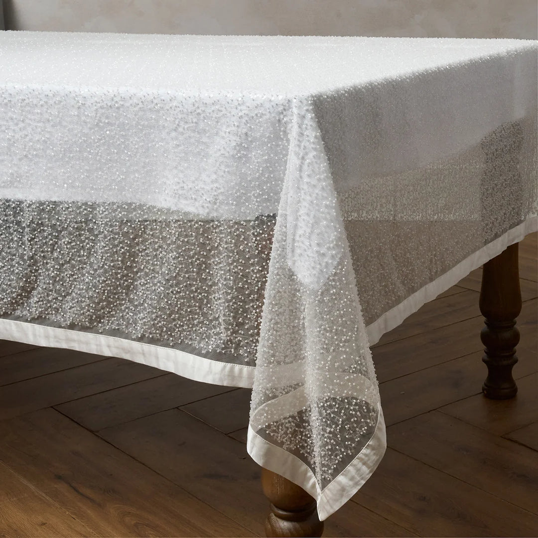 White sequin tablecloth draped over a dining table with sparkling sequins and smooth satin trim