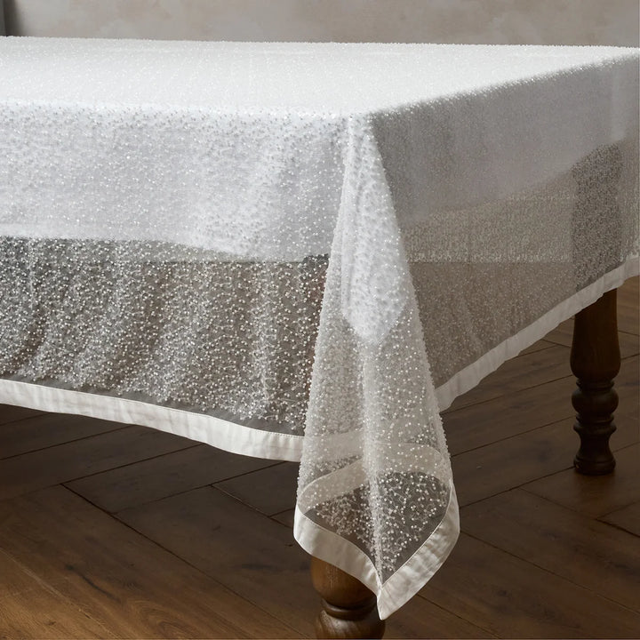 White sequin tablecloth draped over a dining table with sparkling sequins and smooth satin trim
