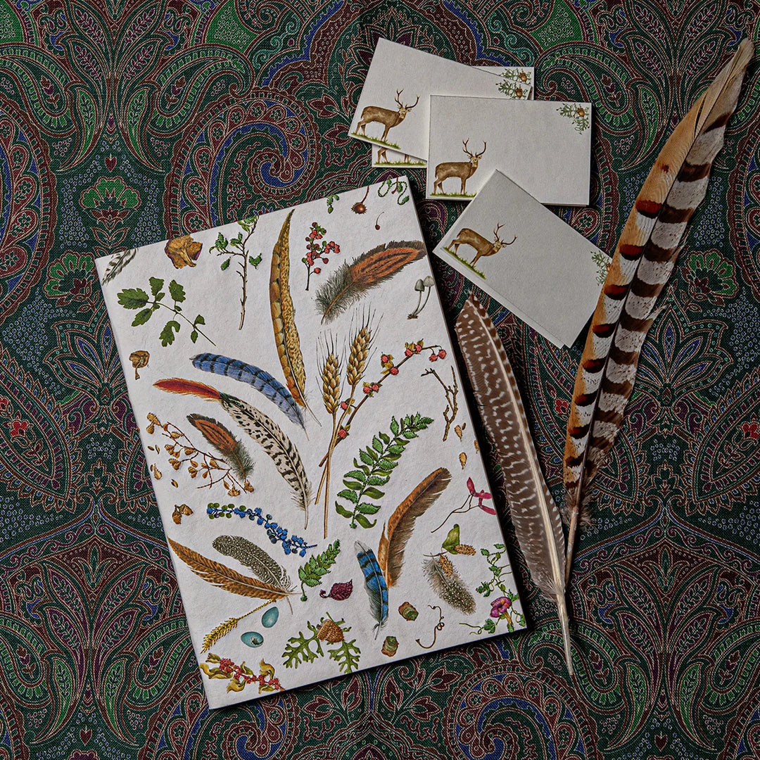 Woodland nature journal with feather and botanical cover displayed with coordinating deer place cards and decorative feathers.