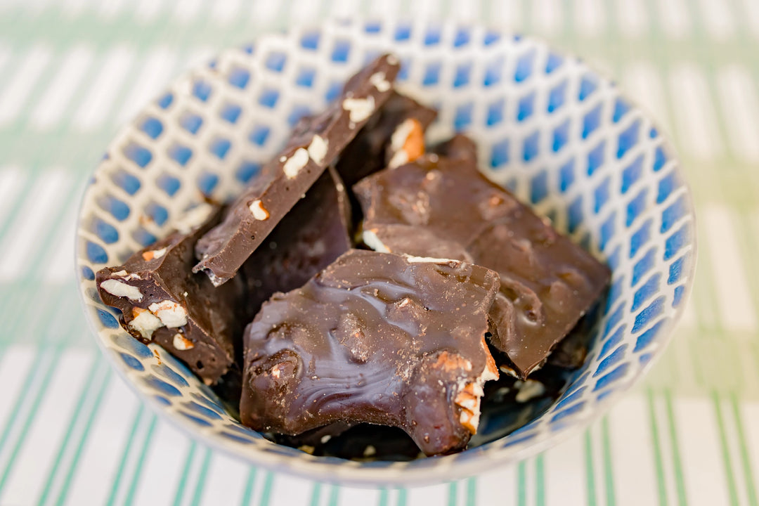 Close-up of rich dark chocolate pecan bark pieces with visible Georgia-grown pecans in a decorative blue ceramic bowl.