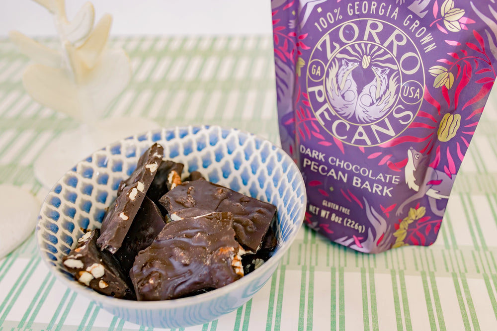 Zorro Dark Chocolate Pecan Bark displayed beside a blue patterned bowl filled with rich dark chocolate and pecan pieces.