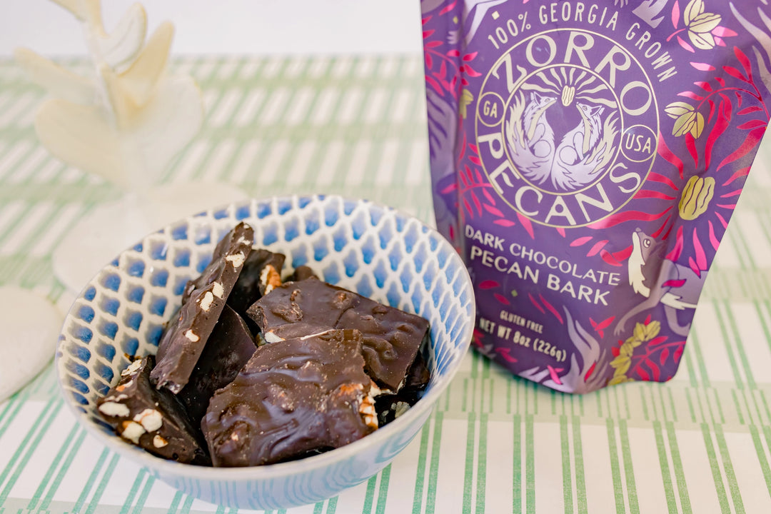 Zorro Dark Chocolate Pecan Bark displayed beside a blue patterned bowl filled with rich dark chocolate and pecan pieces.