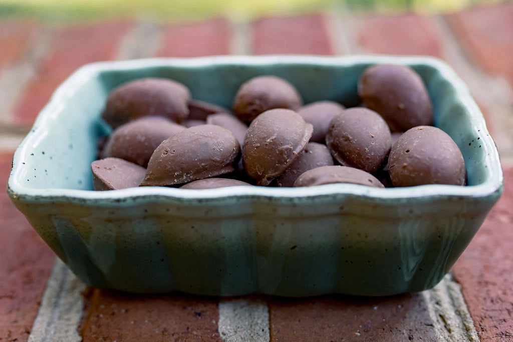 Close-up of rich milk chocolate covered pecans piled in a decorative green ceramic dish, showcasing their smooth chocolate coating.
