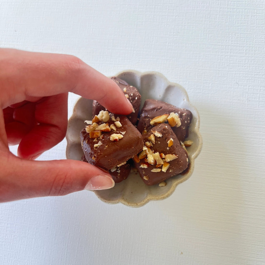 Close-up of milk chocolate pecan toffee pieces topped with chopped pecans in a decorative ceramic bowl.